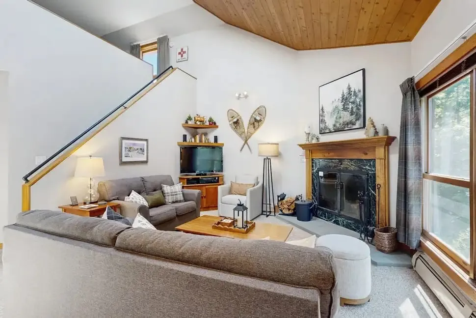 Living room with a wood-burning fireplace, vaulted pine ceiling, and a staircase leading up to the loft