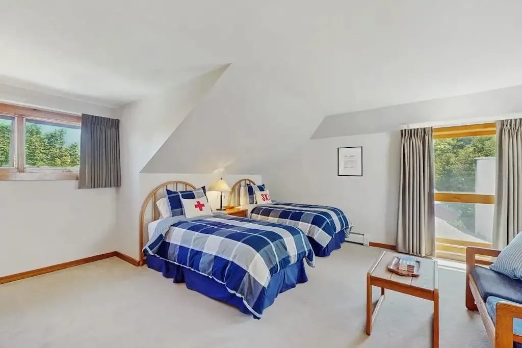 Loft twin beds with red cross and ski-themed pillows near a door leading to the balcony