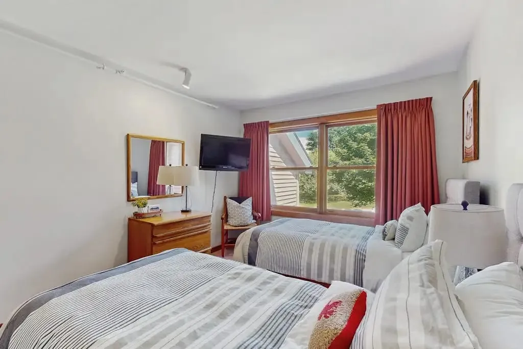 Second bedroom twin beds beside a dresser with mirror and red curtains